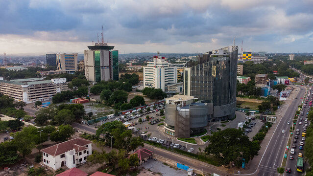 Accra, Ghana - 25 August 2021: Aerial view of the Ecobank Ghana Plc Head Office surrounded by modern office buildings, lush trees, and busy roads under a cloudy sky.
