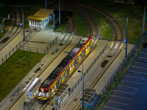 Aerial view of a modern yellow and red tram at a station at night, with illuminated platforms and tracks in Warszawa, Mazowieckie, Poland.