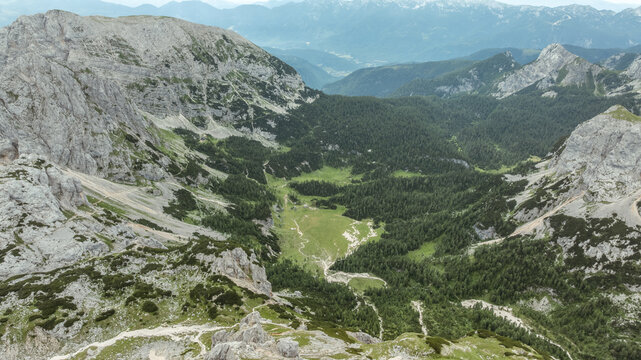 Aerial view of Triglav National Park featuring rugged limestone peaks, lush green alpine valleys, and winding mountain trails in Bohinjsko jezero, Slovenia.