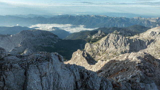 Aerial view of Triglav National Park featuring jagged limestone peaks, deep valleys, and distant clouds over the Julian Alps in Bohinjsko jezero, Slovenia.