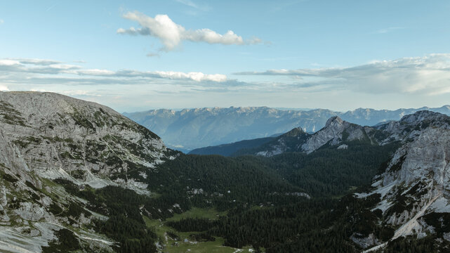Aerial view of Triglav National Park featuring rugged limestone peaks, dense pine forests, and a lush green valley under a clear blue sky in Bohinjsko jezero, Slovenia, Slovenia.