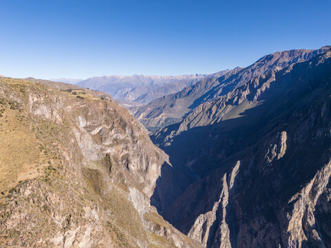 Aerial view of the deep Colca Canyon with rugged rock formations, steep cliffs, and shadows cast across the landscape in Cabanaconde, Arequipa, Peru.