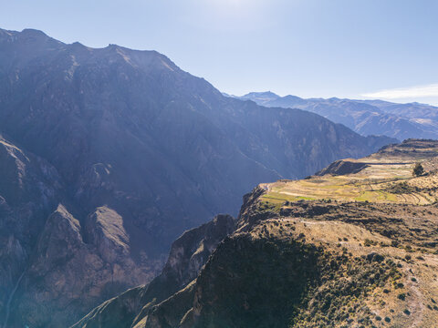 Aerial view of Colca Canyon featuring deep rugged mountain slopes, terraced agricultural fields, and expansive landscape under a clear sky in Cabanaconde, Arequipa, Peru.