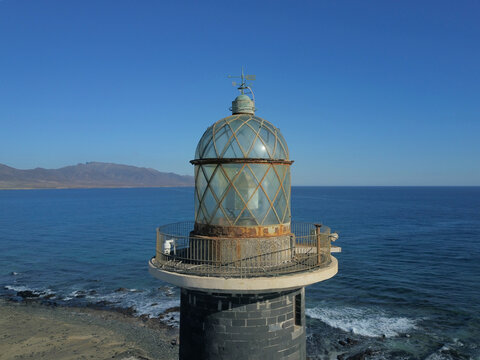 09 January 2019: Aerial view of the lantern room of a lighthouse with a glass dome and metal railing, overlooking the calm blue sea and distant mountains under a clear sky.
