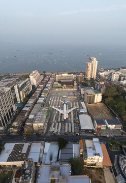 Aerial view of a large airplane landmark surrounded by rows of market stalls and urban buildings near the coastline in Pattaya City, Chon Buri, Thailand.