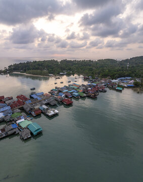 Aerial view of Bang Bao Pier featuring colorful stilt houses over the water, surrounded by lush green hills and calm sea in Koh Chang, Trat, Thailand.