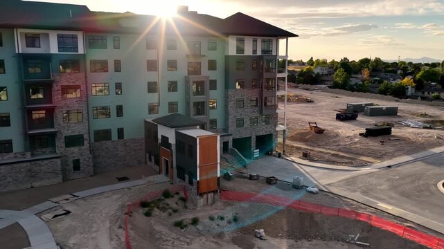 Aerial view of a new apartment complex construction site with stone and siding facade, paved parking area, and surrounding dirt landscape in Taylorsville, Utah, United States.