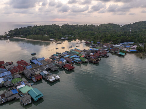 Aerial view of Bang Bao Pier featuring colorful stilt houses over the calm bay with lush green hills in the background at sunset in Koh Chang, Trat, Thailand.