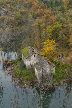 Aerial view of the ruins of stone buildings at Lago di Poggio Baldi surrounded by autumn foliage and dead trees in the water with people nearby in Santa Sofia, Emilia-Romagna, Italy.