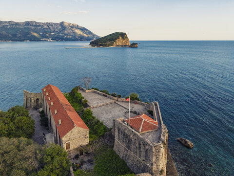 Aerial view of the historic Budva Citadel with its stone walls and red-tiled roofs overlooking the Adriatic Sea and the island of Sveti Nikola in Budva, Budva Municipality, Montenegro.
