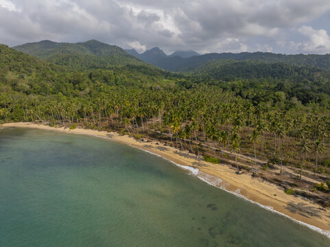 Aerial view of Wai Chaek Beach with lush palm trees and green mountains along the turquoise coastline in Koh Chang Tai, Trat, Thailand.