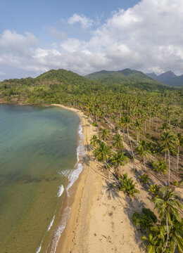 Aerial view of Wai Chaek Beach featuring golden sands, turquoise waters, and a dense forest of palm trees under a bright sky in Koh Chang Tai, Trat, Thailand.