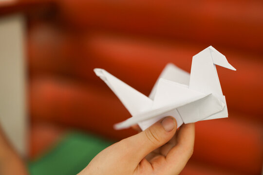 Child hands holding origami crane on red background symbolizing peace