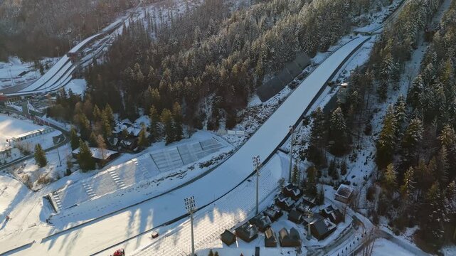 Aerial view of Zakopane ski jumping stadium and snowy ski slopes in Lesser Poland, with grandstands, forested hillsides and mountain scenery in winter.