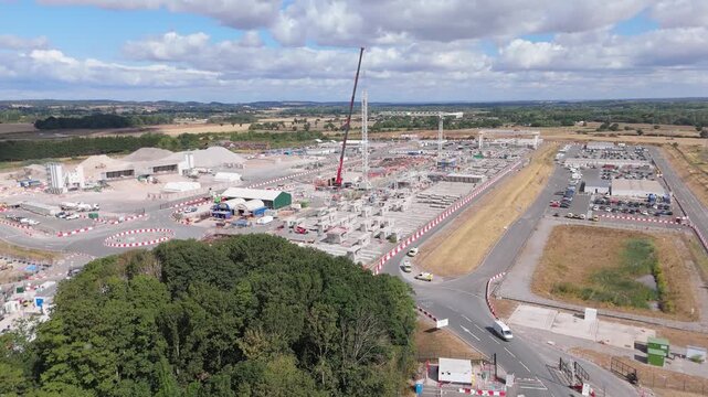 A drone pullback view of a site storage compound for a high speed railway currently being constructed showing materials available, cranes and transport