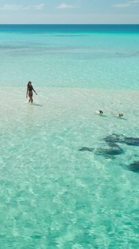 Breathtaking aerial view of a young woman enjoying a leisurely walk on a pristine sandbank, her friend swimming in the crystal-clear turquoise waters of the maldives