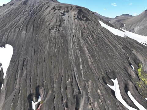 Aerial view of Raudufossafjoll volcanic mountain featuring dark volcanic soil, deep erosion gullies, and patches of snow under a clear blue sky in Hella, Rangarthing ytra, Iceland.