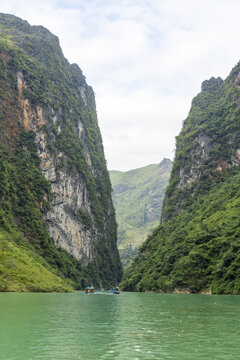View of the Nho Que River winding through the towering limestone cliffs of the Ha Giang Loop with small boats navigating the turquoise water in Dong Van, Tuyen Quang, Vietnam.