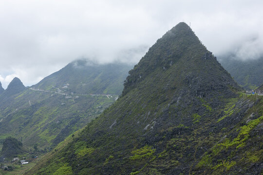 View of Ha Giang Loop with winding mountain roads, lush green slopes, and misty clouds in Dong Van, Tuyen Quang, Vietnam.