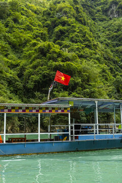 View of a traditional boat with a Vietnamese flag floating on a river against a backdrop of lush green mountains along the Ha Giang Loop in Dong Van, Tuyen Quang, Vietnam.
