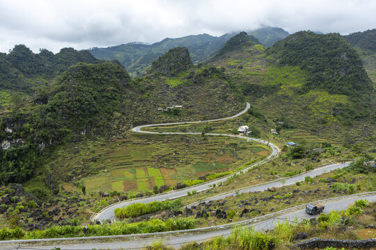 View of the winding Ha Giang Loop road cutting through the dramatic rocky mountains and terraced fields in Dong Van, Tuyen Quang, Vietnam.