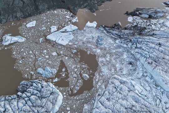 Aerial view of the icy surface of Falljokull glacier with deep crevasses and floating ice chunks in the glacial lagoon, Svinafell, Sveitarfelagid Hornafjordur, Iceland.