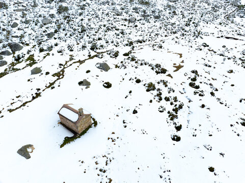 Aerial view of Capela de Santo Antonio surrounded by a snow-covered landscape with scattered rocks and sparse vegetation in Manteigas, Distrito da Guarda, Portugal.