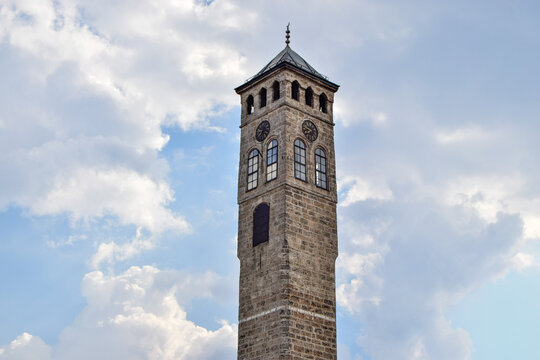 View of the historic stone clock tower with arched windows and a clock face set against a blue sky with white clouds in Mostar, Federation of Bosnia, Bosnia and Herzegovina.