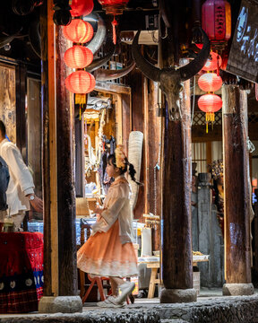 Xiangxi Tujia and Miao Autonomous Prefecture, Hunan, China - 23 March 2024: View of a girl in traditional dress walking through Furong Town, decorated with red lanterns and wooden pillars.
