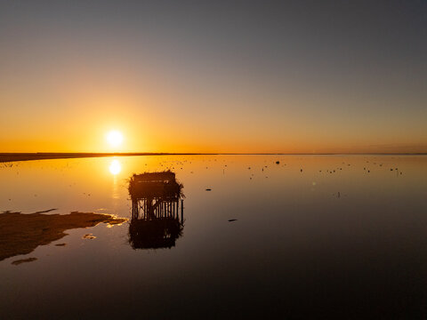 Aerial view of a hunting blind in Lake Ellesmere Te Waihora at sunset with calm water reflecting the golden light in Canterbury Region, New Zealand.