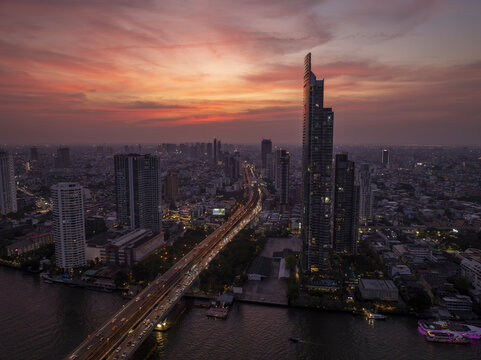 Aerial view of the Bangkok skyline at sunset with skyscrapers, the Chao Phraya River, and a busy highway bridge in Bangkok, Bangkok, Thailand.