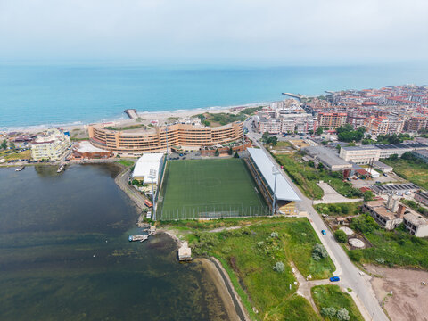 Aerial view of Pomorie Stadium located between the Black Sea and the town, featuring the green pitch, stadium lights, and coastal buildings in Pomorie, Burgas, Bulgaria.