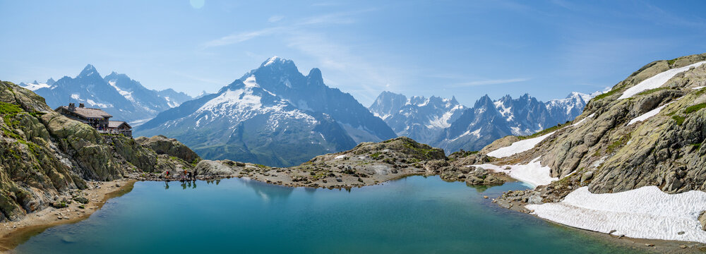 View of the turquoise waters of Lac Blanc reflecting the snow-capped peaks of the Mont Blanc massif, with rocky terrain and hikers in the background in Chamonix, Auvergne-Rhone-Alpes, France.
