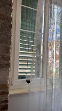 A glass of red wine on a windowsill with lace curtains and stone wall