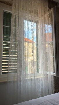 Lace curtains hanging on an open window with a view of old European stone buildings