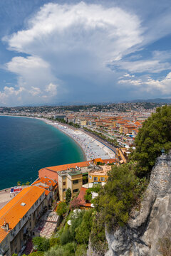 View of the Mediterranean coastline and Promenade des Anglais, featuring historic buildings, a crowded beach, and a dramatic cloud in Nice, Provence-Alpes-Cote d'Azur, France.