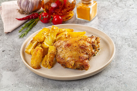 Roasted chicken thigh with spiced potato wedges and herbs on plate