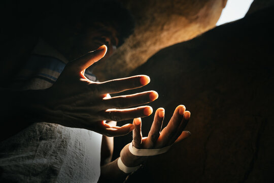 View of a person's hands illuminated by soft light inside a dark, rocky cave in Hampi, Karnataka, India.