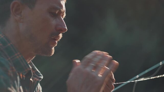 Young adult fisherman fly fishing on the river. Man blows and dries the fishing fly after it got wet in the water