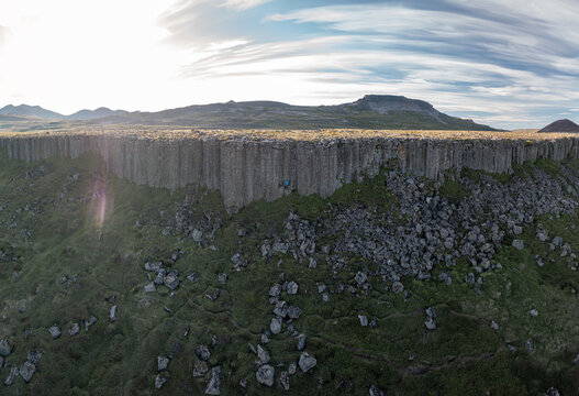 Aerial view of Gerduberg Cliffs featuring hexagonal basalt columns rising above a grassy slope with scattered rocks under a bright sky Raudhamelur, Eyja- og Miklaholtshr, Iceland.