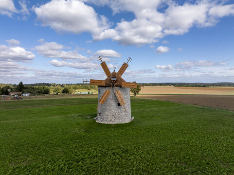Aerial view of the historic Regi Szelmalom windmill with its wooden blades set in a vibrant green field under a blue sky with scattered clouds in Tes, Hungary.