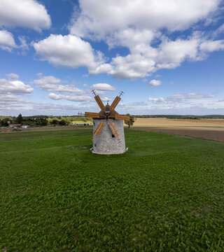 Aerial view of the historic Regi Szelmalom windmill standing in a green field under a blue sky with clouds in Tes, Hungary.