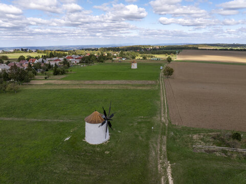 Aerial view of the historic Regi Szelmalom windmills situated in the green fields near the village, with cultivated farmland and a blue sky with clouds, Tes, Hungary.