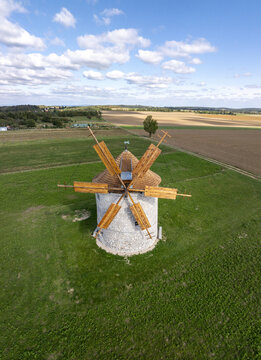 Aerial view of the historic Regi Szelmalom windmill, featuring its stone structure and wooden blades, set amidst green fields and agricultural land in Tes, Hungary.