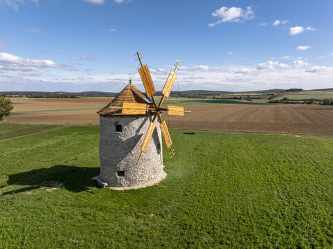 Aerial view of the historic Regi Szelmalom windmill standing in a green field surrounded by agricultural farmland under a blue sky in Tes, Hungary.