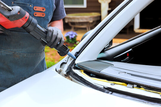 Handy worker repairs car window seal using tool outside near house