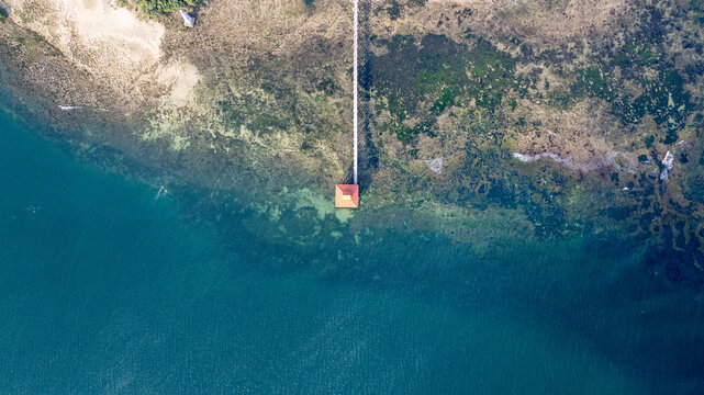 Aerial view of a long pier extending into the turquoise waters of the Indian Ocean, featuring a small structure at the end and a rocky coastline in Mombasa, Mombasa County, Kenya.