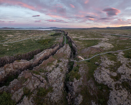 Aerial view of Thingvellir National Park featuring the tectonic rift valley with volcanic rock, mossy terrain, and walking paths under a sunset sky in Selfoss, Blaskogabyggd, Iceland.