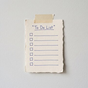 Handwritten to do list on a piece of textured paper taped to a plain white wall background