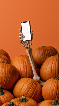 A skeleton hand holds a phone against a background of pumpkins. Halloween advertisement.